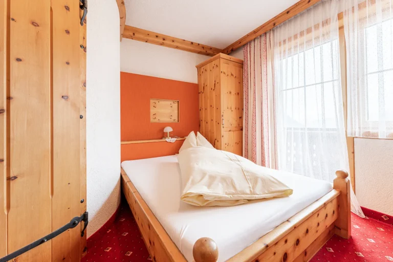Einzelzimmer mit warmer Farbgestaltung, Holzbett und hellem Fenster im familiengeführten Sagritzer Wirt in Großkirchheim